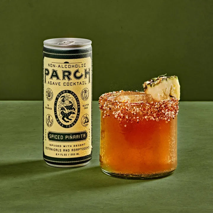 Non-alcoholic PARCH agave cocktail can next to a glass of spiced pineapple cocktail on a green background