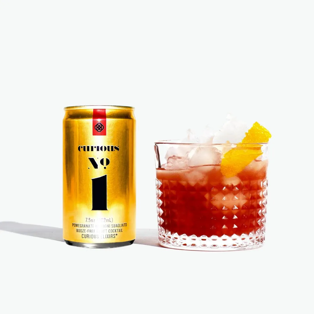 Gold can labeled 'Curious 1' next to a cocktail with ice and a pineapple wedge on a white background