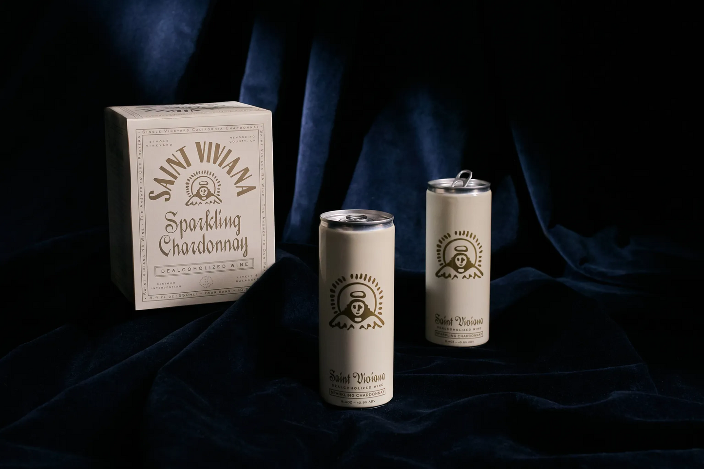 Saint Viviana sparkling wine packaging including a box and two cans on a dark fabric background