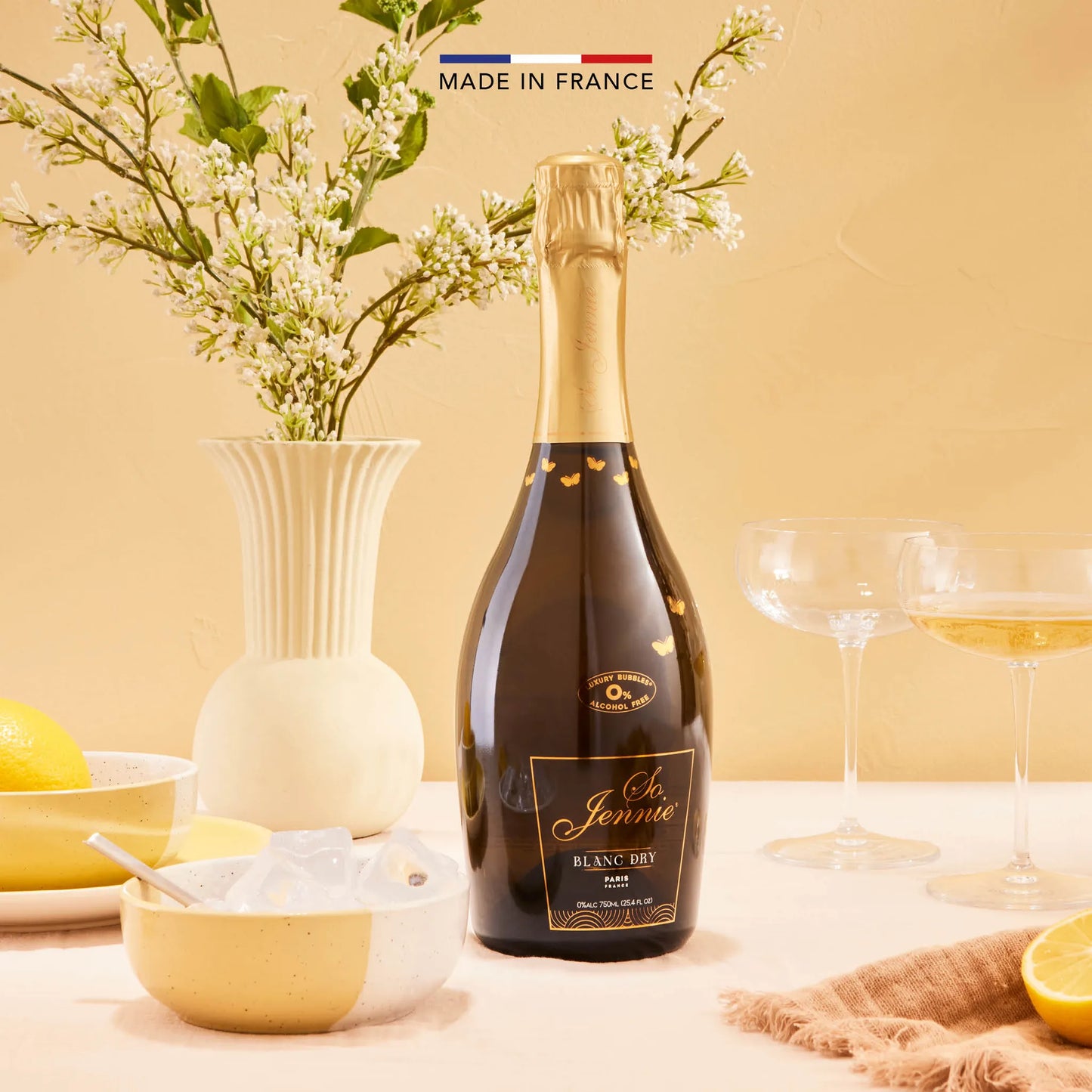 Bottle of NA champagne on a table with flowers and glasses, set against a beige background.