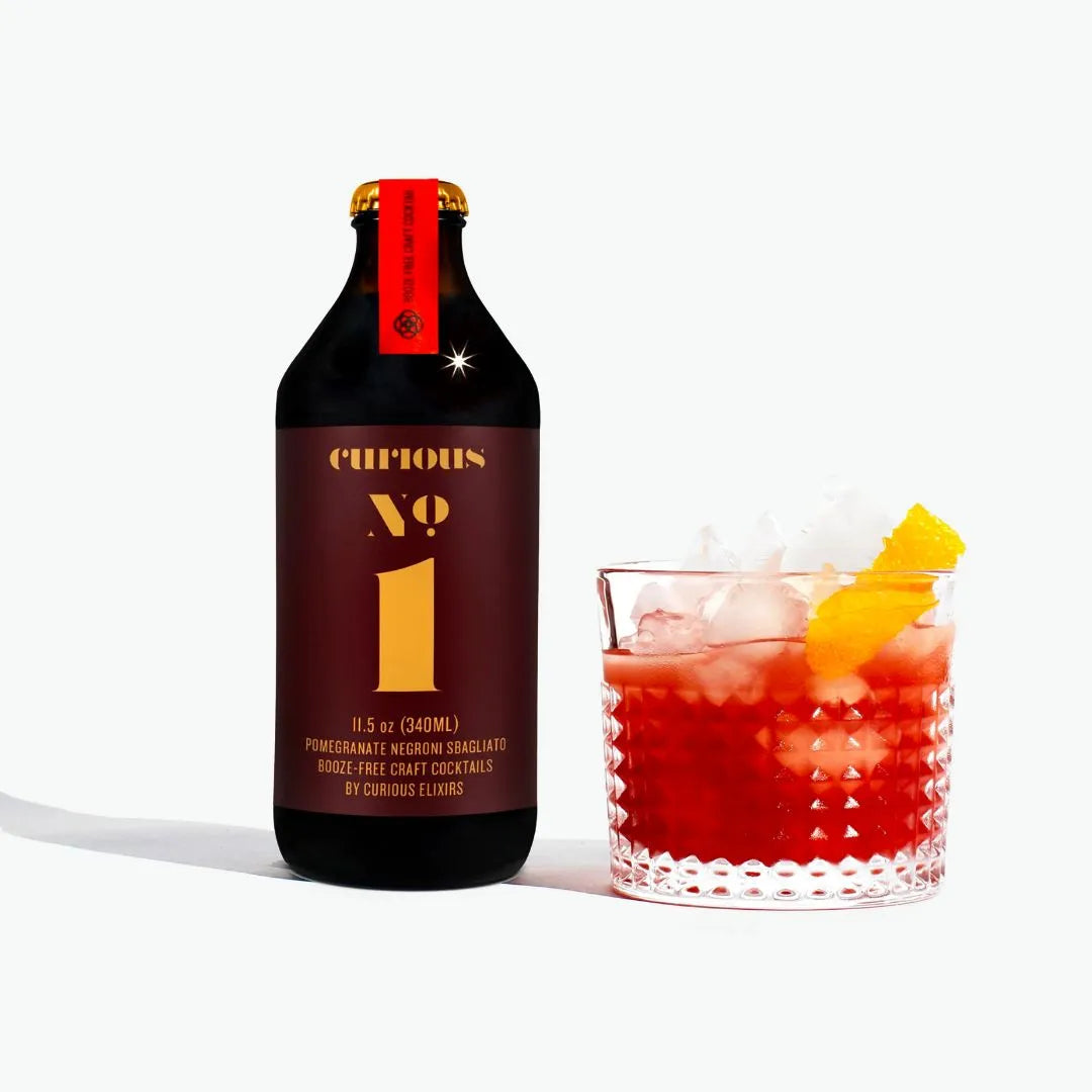 Bottle of Curious No. 1 cocktail with a glass of red cocktail with ice and a slice of orange on a white background