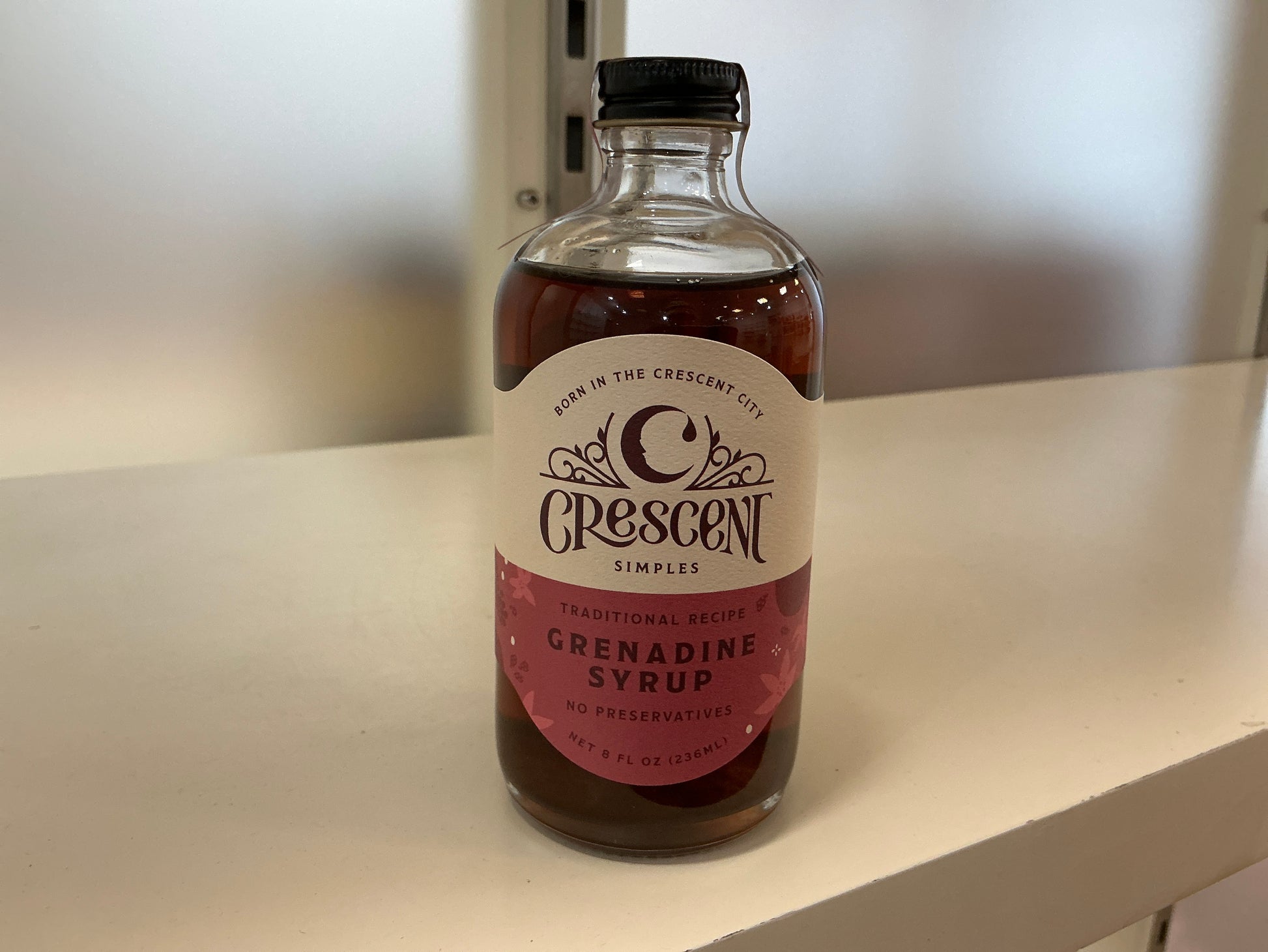 Bottle of Crescent Grenadine Syrup on a white surface with a blurred background