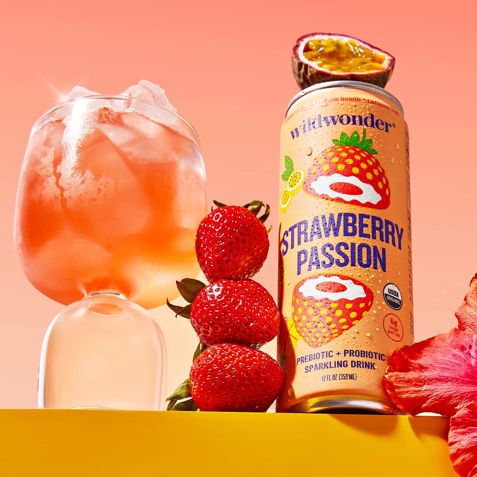 Can of Wild Wonder Strawberry Passion drink with a glass of pink drink and strawberries on a peach background