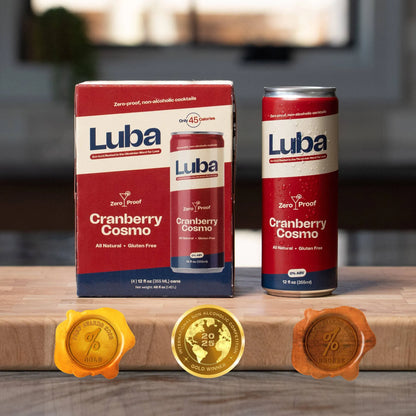 Luba Cranberry Cosmo drinks on a wooden surface with product packaging and gold seals.