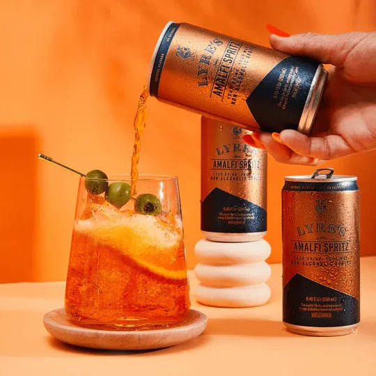 Person pouring Lyres Amalfi Spritz into a glass with an orange background