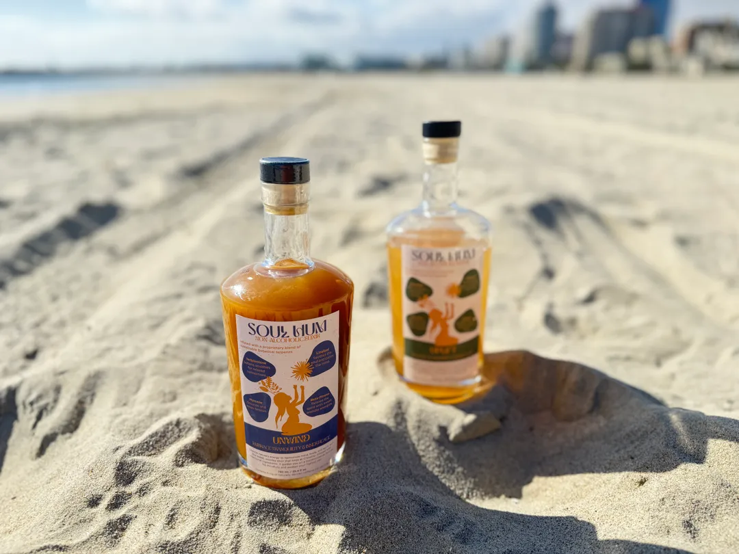 Two bottles on a sandy beach with a cityscape in the background.
