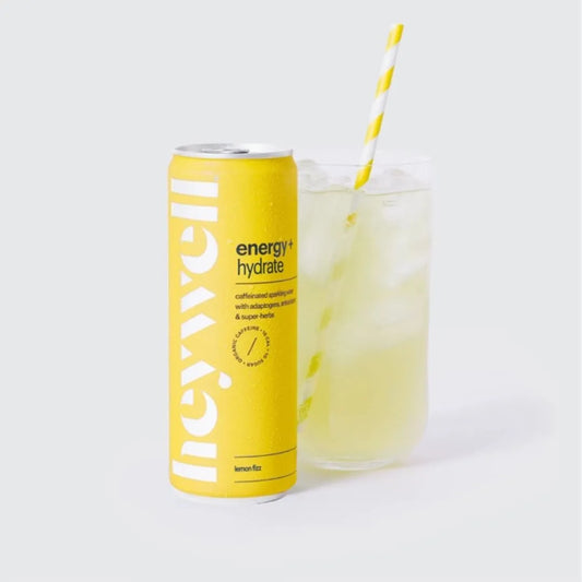 Yellow energy drink can labeled 'energy + hydrate' next to a glass of lemonade with a straw on a light gray background.