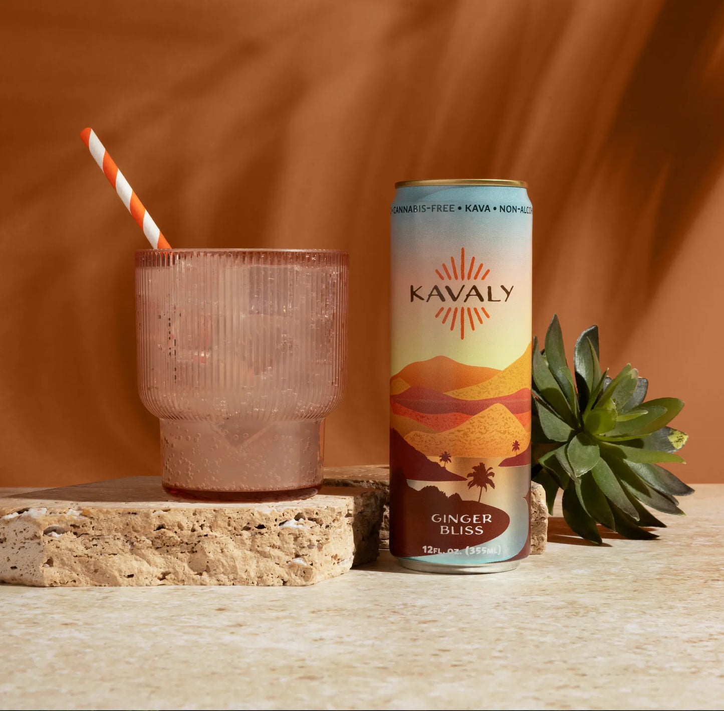 Kavaly Ginger Bliss can with a glass and straw on a wooden surface against an orange background