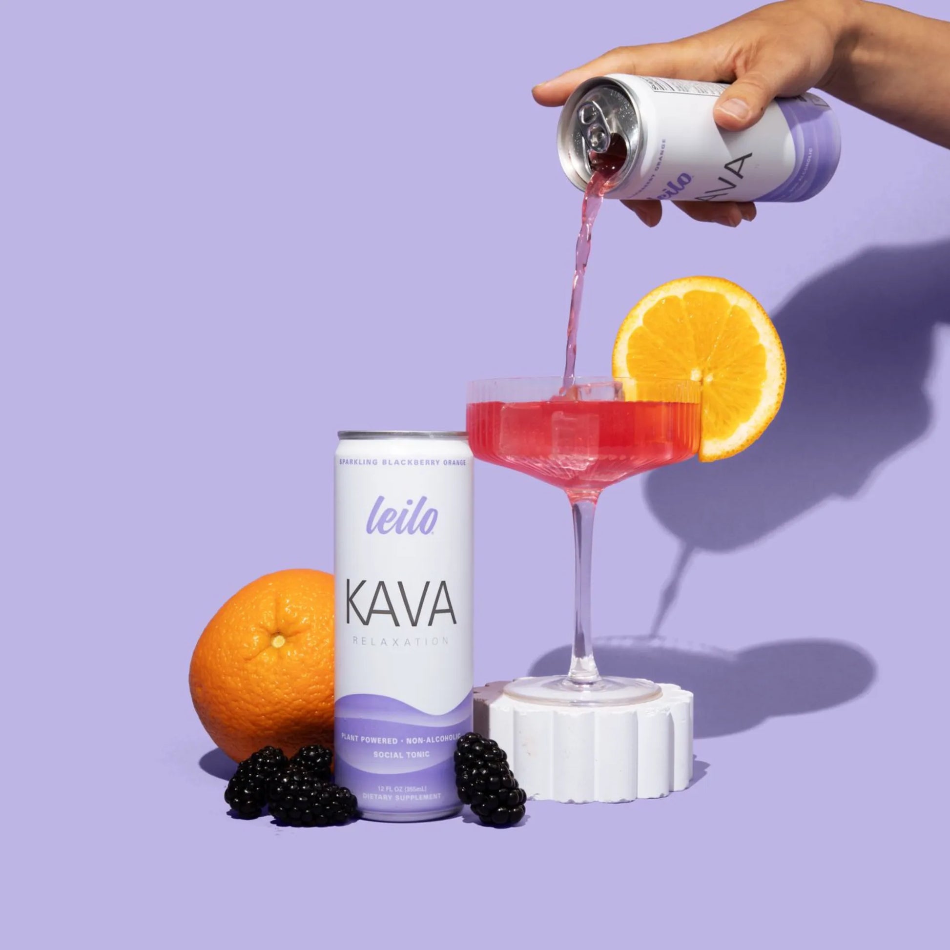 Person pouring Kava drink from a can into a glass with an orange slice on a purple background