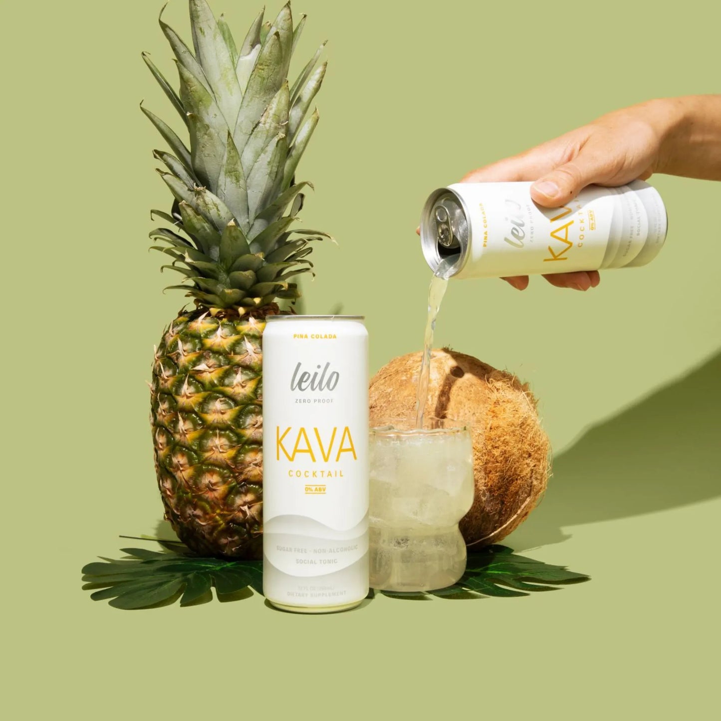 Person pouring KAVA drink from can into glass with pineapple, coconut, and leaf on green background