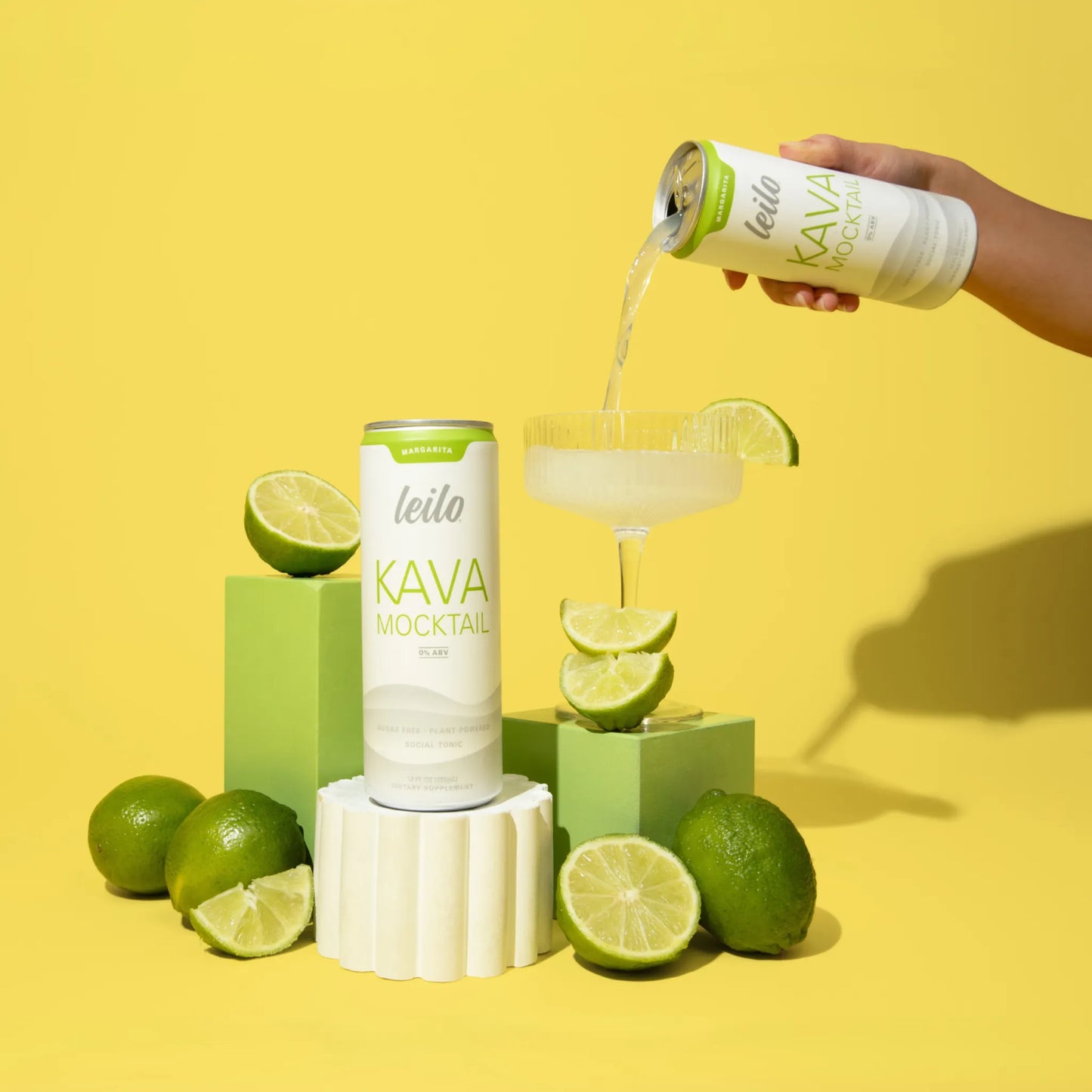 Leito Kava Mocktail can being poured into a glass with lime slices on a yellow background