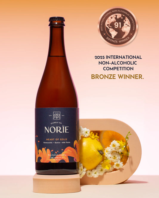 Bottle of Norie 'Heart of Gold' non-alcoholic beer with a decorative plate and flowers on a peach background.