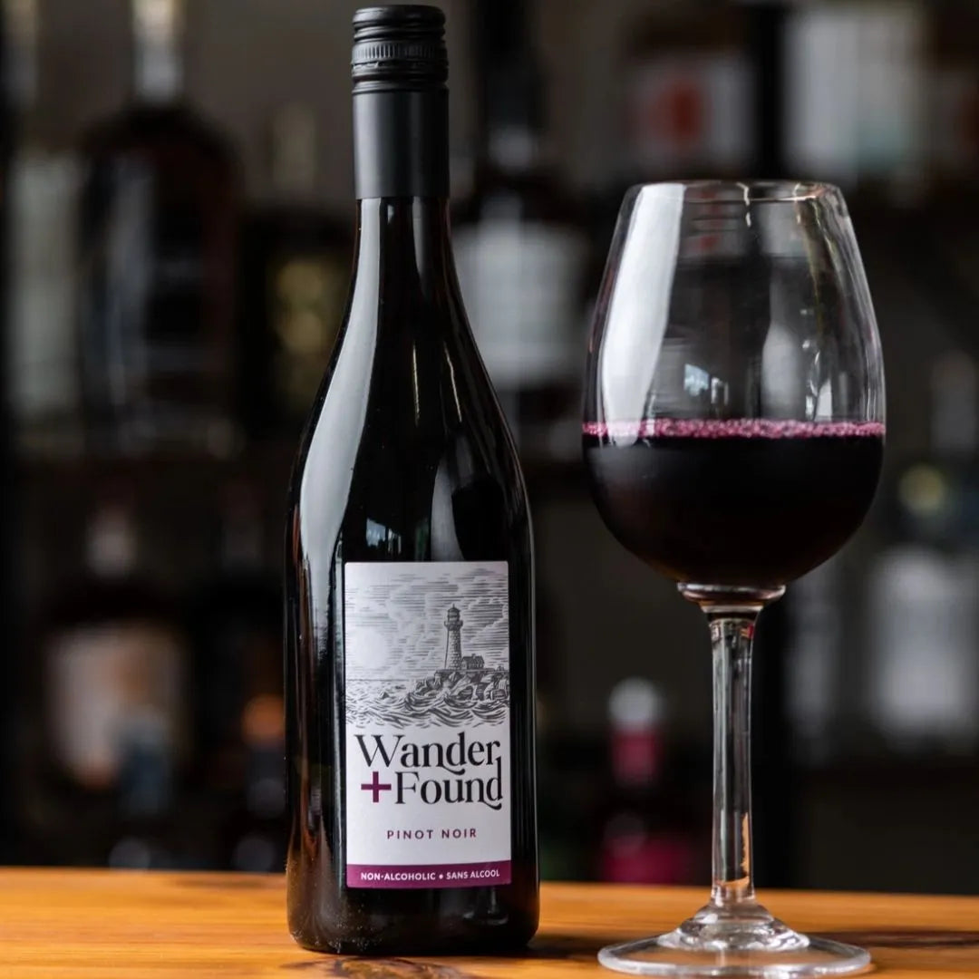 Wander Found non-alcoholic pinot noir bottle and glass on a wooden surface with blurred bar background
