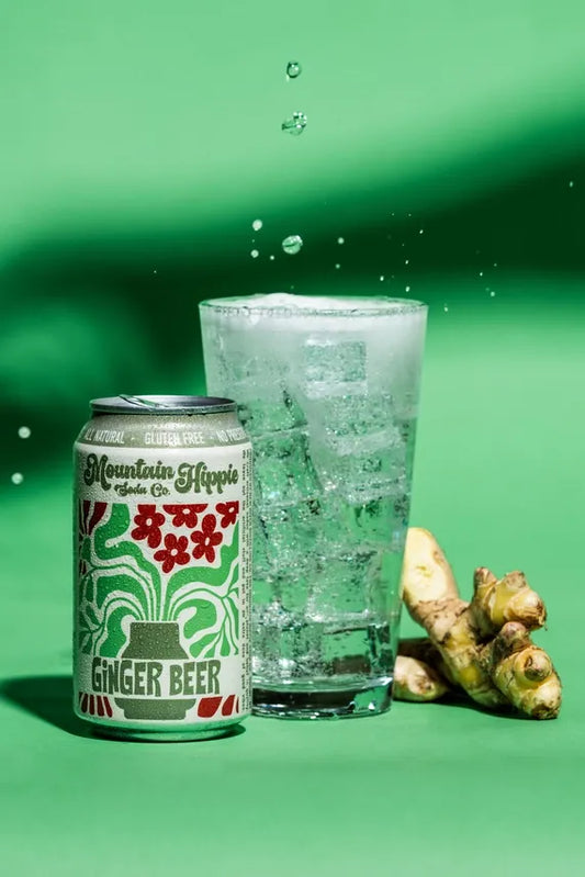 Can of Mountain Hippie Ginger Beer with a glass of ginger beer and ginger root on a green background