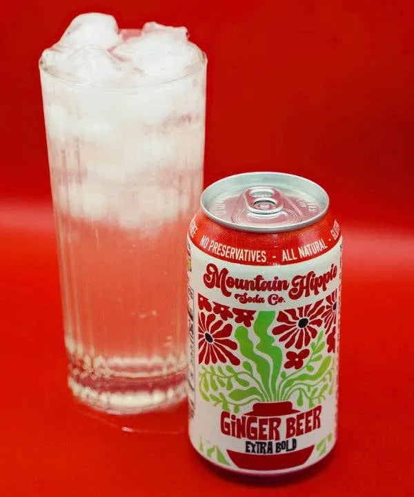 Can of Mountain Hippie Soda Co. Ginger Beer next to a glass with ice on a red background
