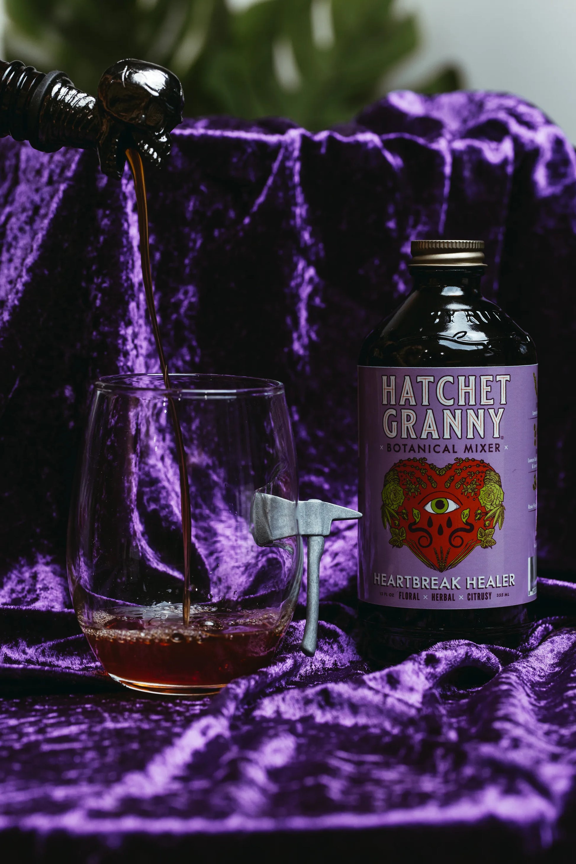 Bottle of Hatchet Granny botanical mixer with a glass on a purple textured surface