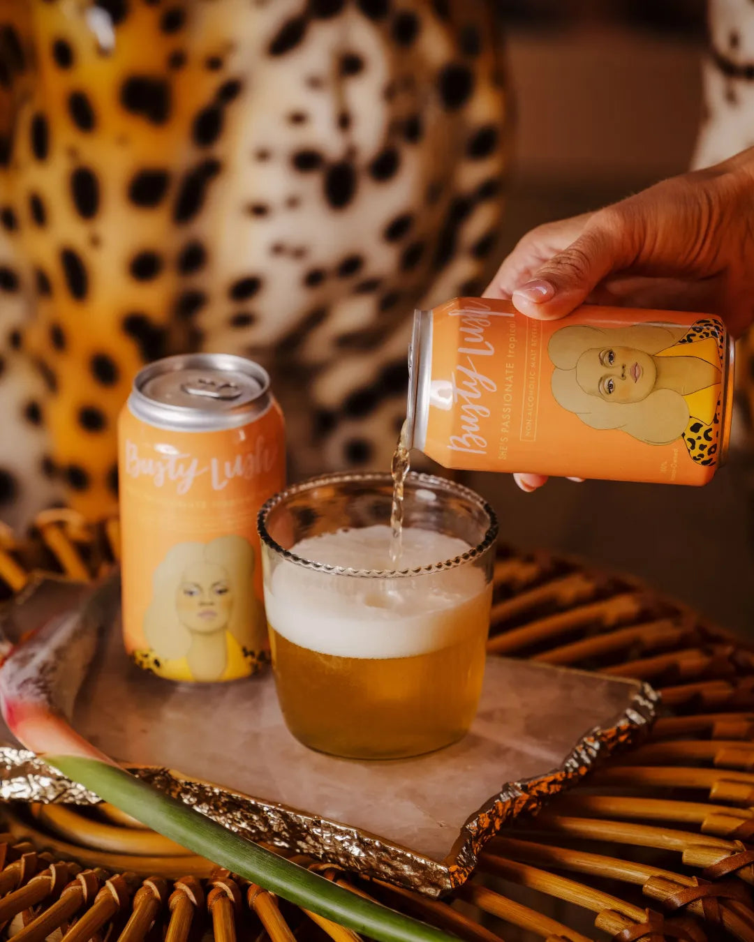 Person pouring a drink from a can into a glass with another can on a tray.