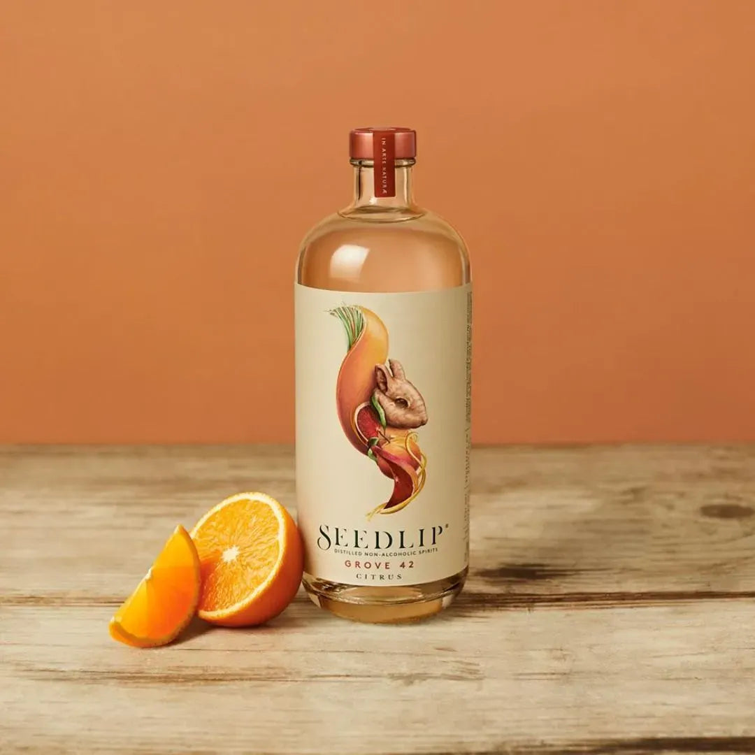 Bottle of Seedlip gin with orange slices on a wooden surface and orange background