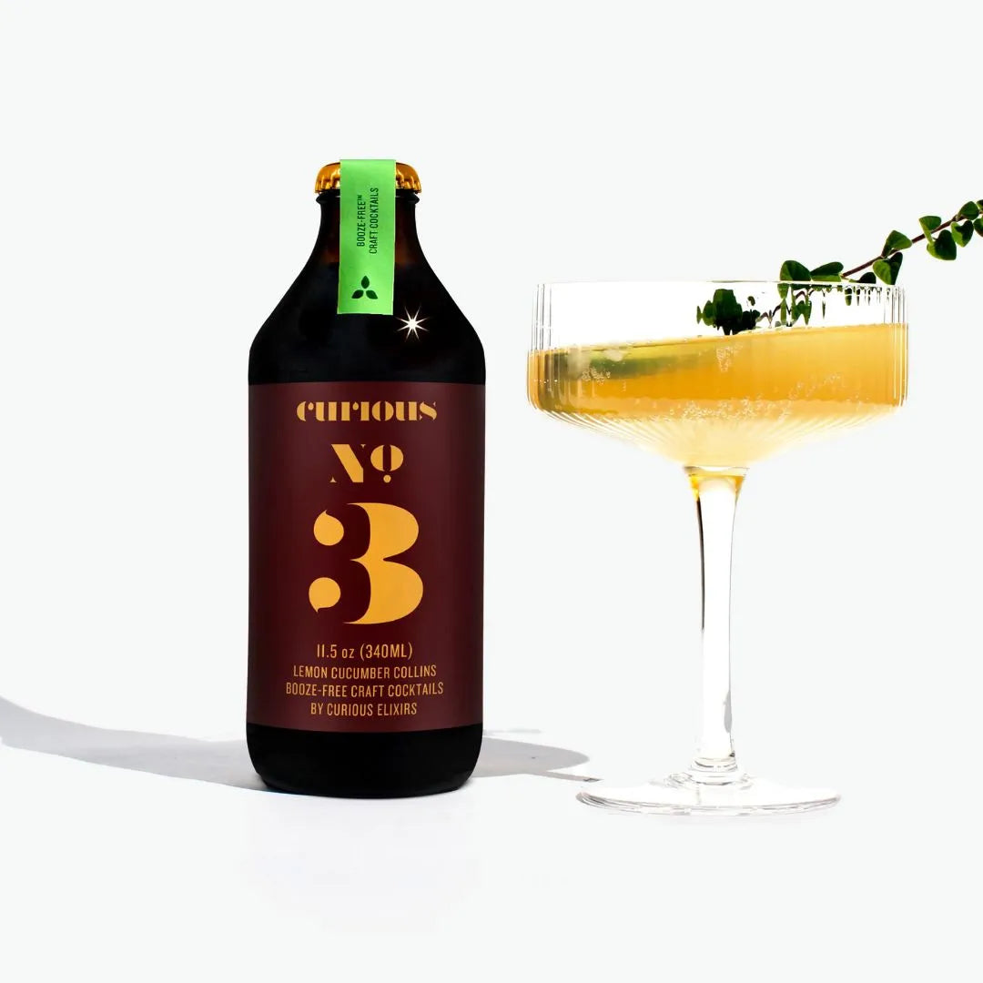 Bottle of Curious No. 3 cocktail with a glass of yellow cocktail on a white background