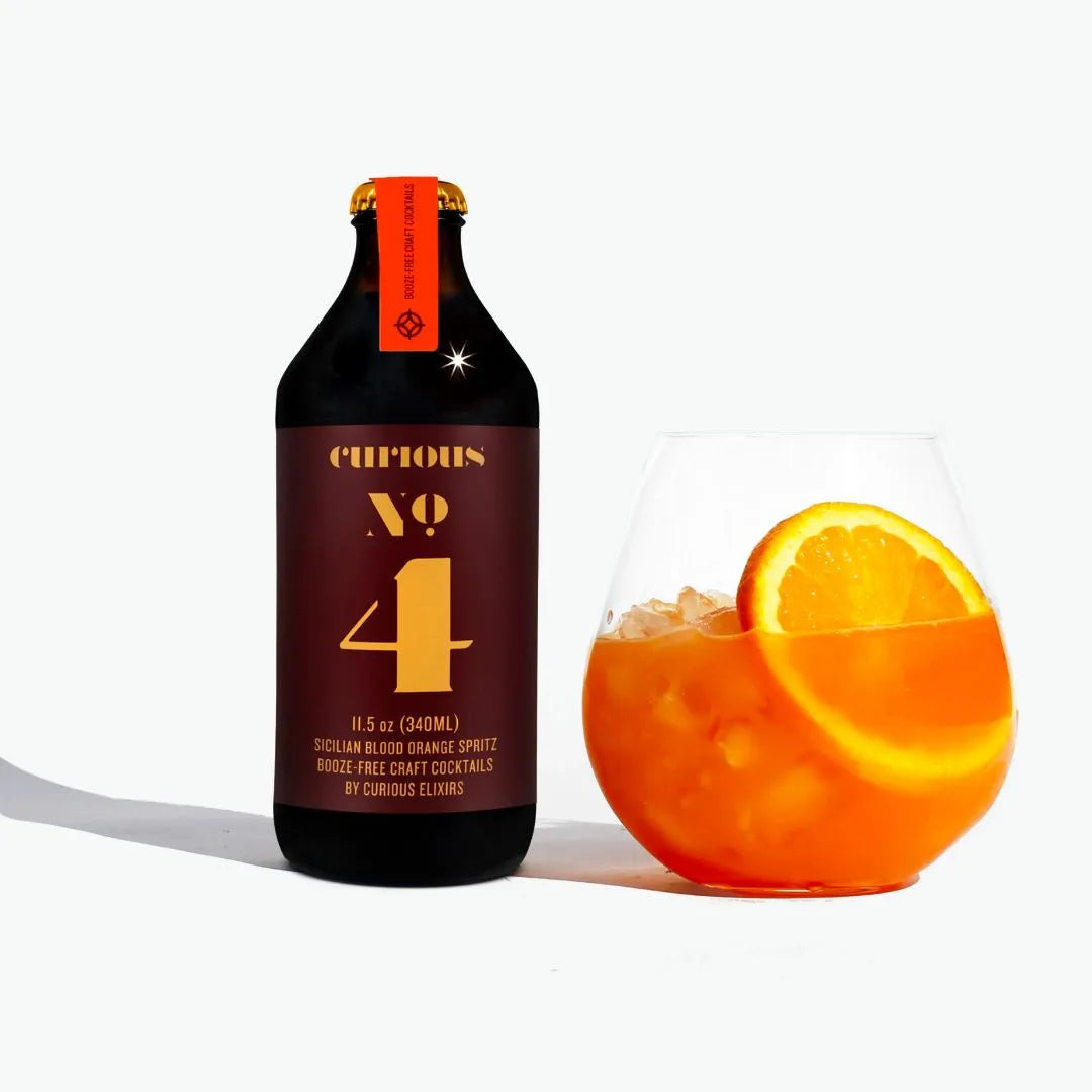 Bottle of Curious No. 4 Sicilian Blood Orange Spritz with a glass of the cocktail and an orange slice on a white background
