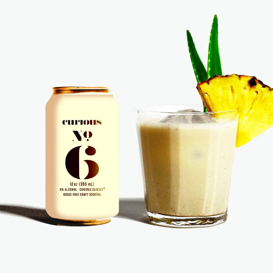 Curious No 6 can next to a glass of pineapple smoothie with a pineapple wedge on a white background