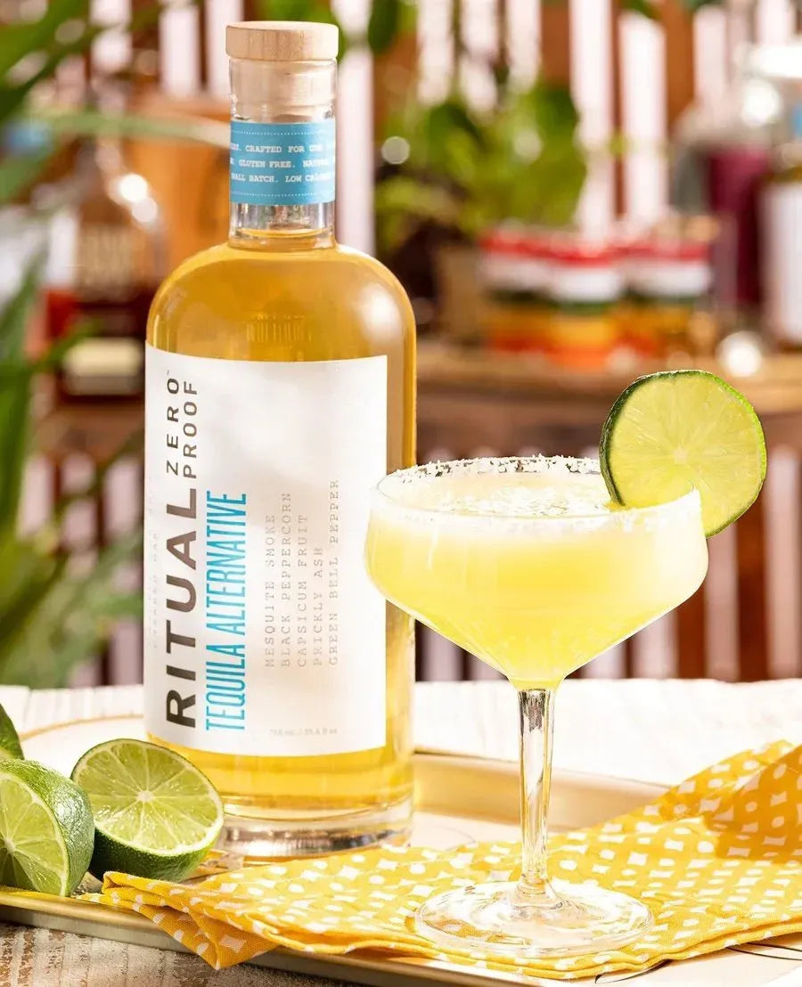 Bottle of Ritual Zero Proof Tequila Alternative with a margarita and lime garnish on a table.