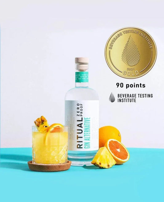 Bottle of Ritual Zero Proof Gin with a cocktail and garnishes on a blue surface, featuring a gold medal award from the Beverage Testing Institute.