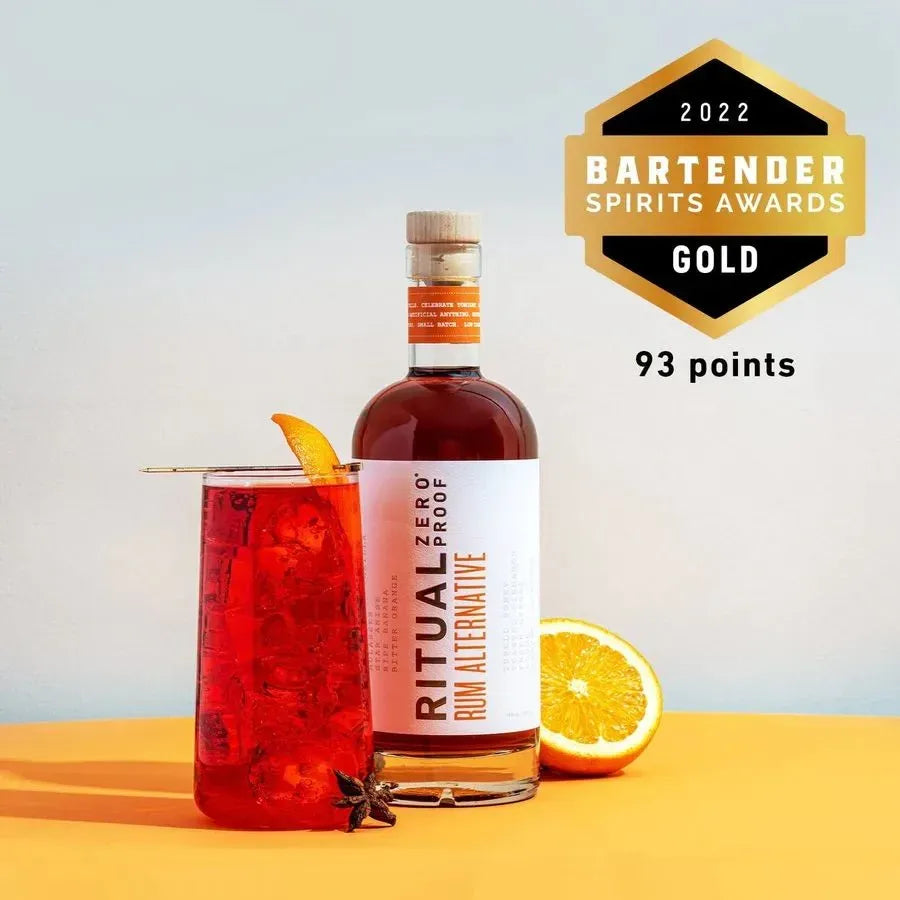 Bottle of Ritual Zero Proof Rum Alternative with a cocktail and orange slice on a yellow surface, featuring a 2022 Bartender Spirits Awards gold medal.