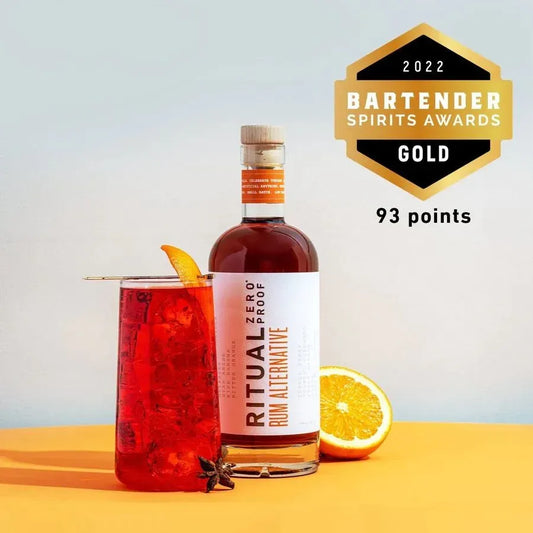 Bottle of Ritual Zero Proof Rum Alternative with a cocktail and orange slice on a yellow surface, featuring a 2022 Bartender Spirits Awards gold medal.