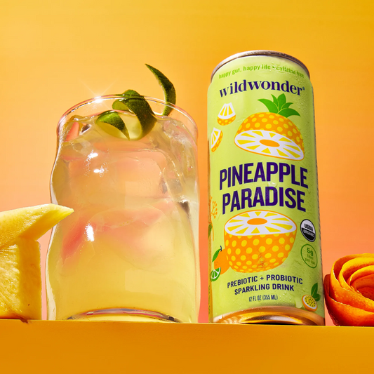 Can of Wildwonder Pineapple Paradise sparkling drink with a glass of pineapple juice on an orange background
