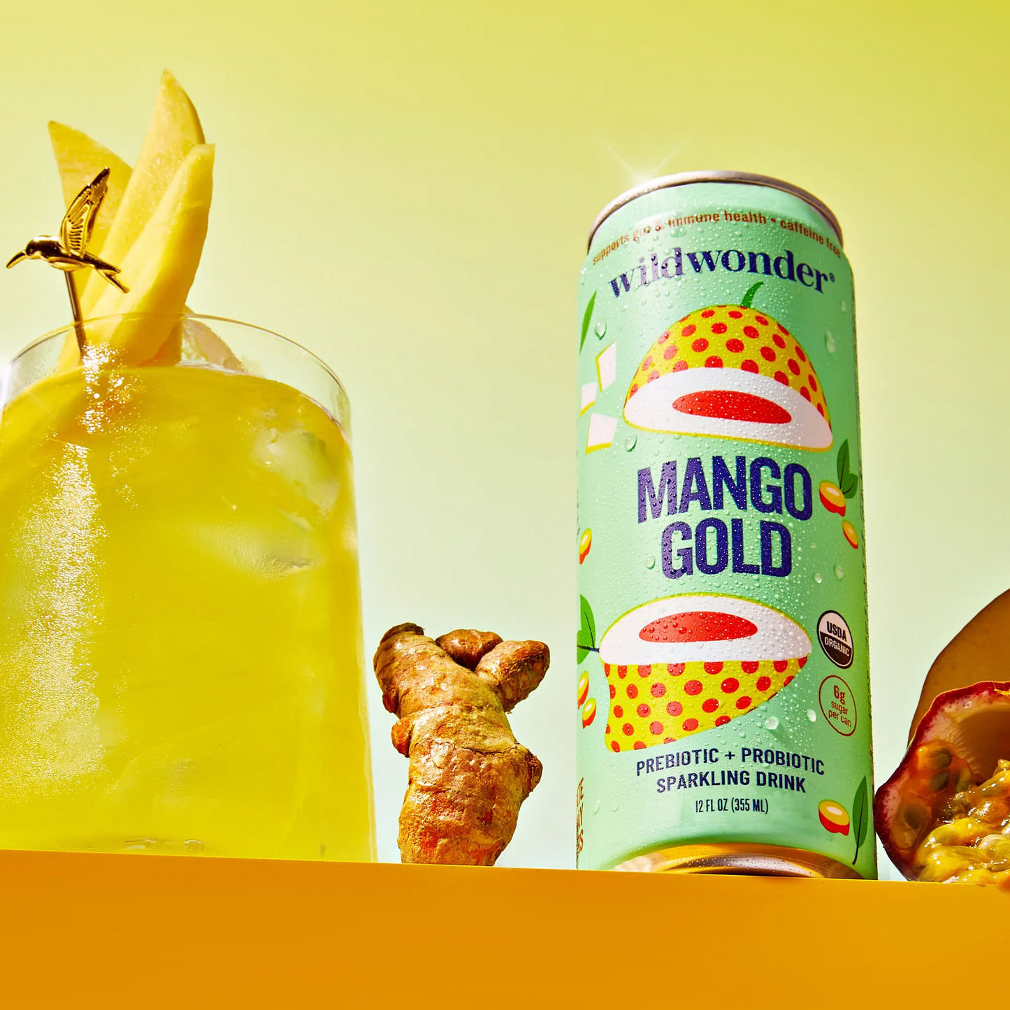 Mango Gold sparkling drink can with a glass of yellow drink and ingredients on a yellow background