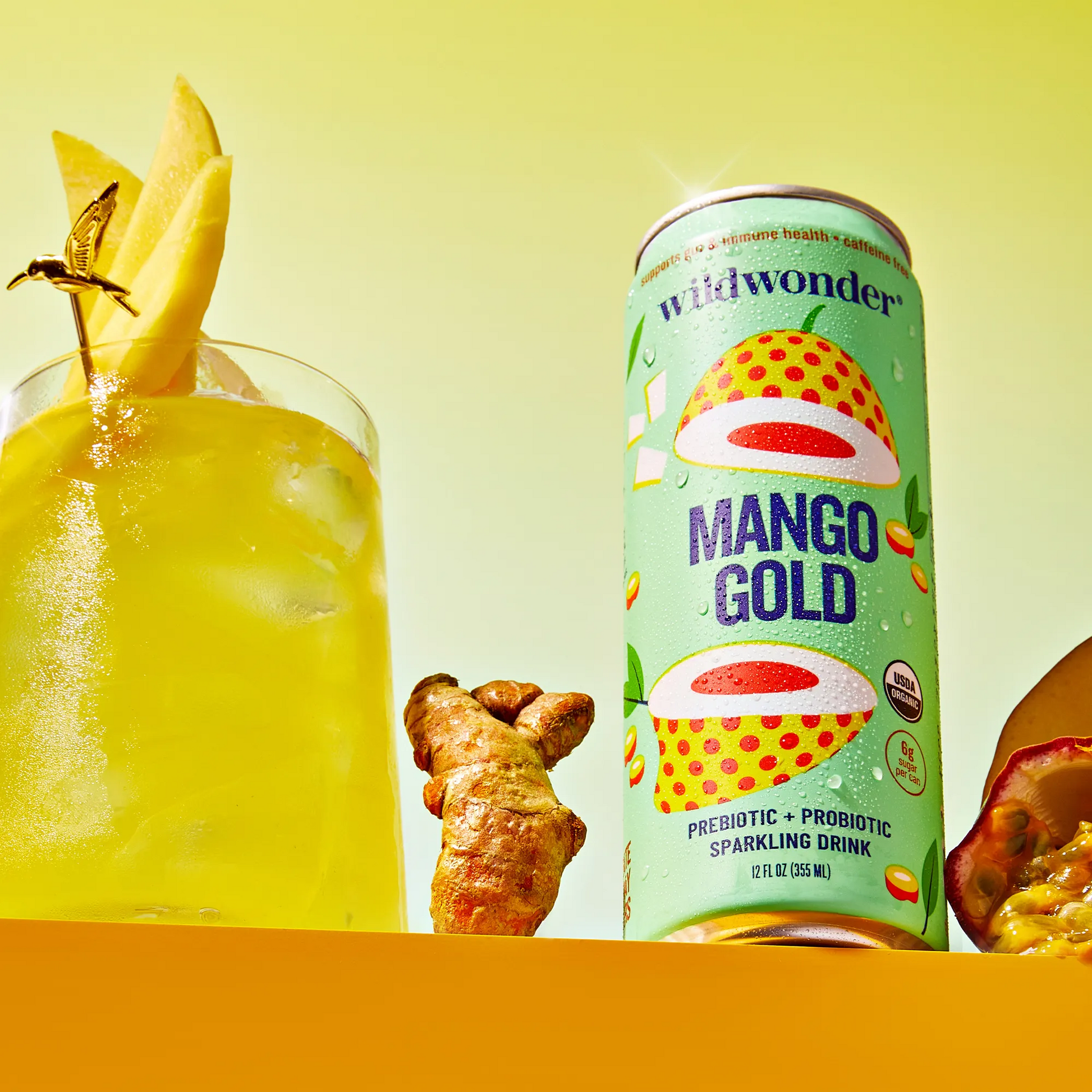 Mango Gold sparkling drink can with a glass of yellow drink and ingredients on a yellow background