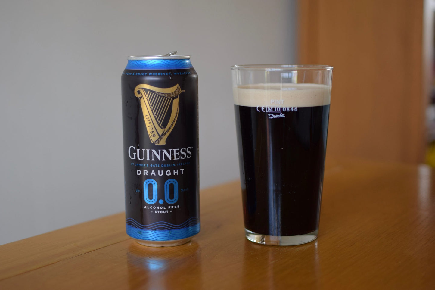 Guinness Draught 0.0 can and glass of dark beer on a wooden surface