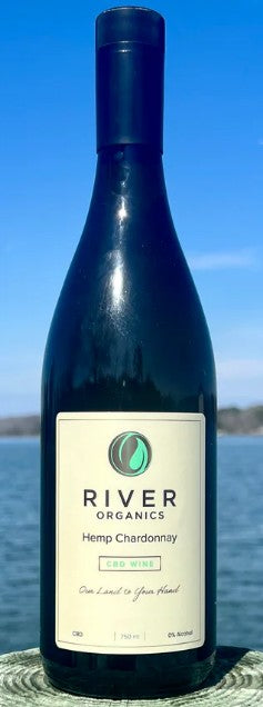 A bottle of River Organics Hemp Chardonnay CBD wine, featuring a dark glass bottle and cream-colored label, set against a background of blue sky and water.