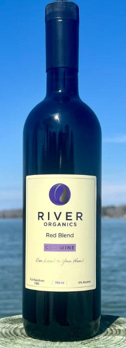 A bottle of River Organics Red Blend Climb Wine standing upright outdoors against a blue sky and water background.